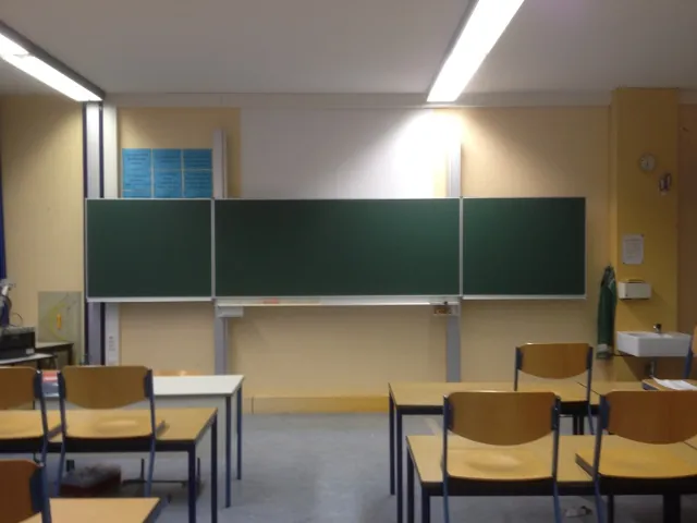 Klassenzimmer mit aufgeklappter grüner Schultafel