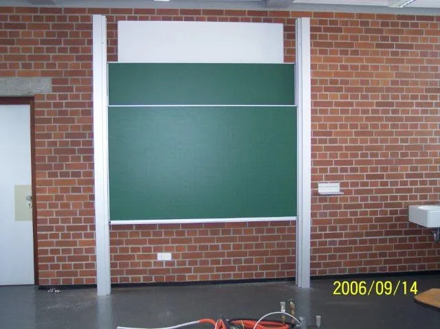 Grüne Kreidetafel an weißen Schienen vor einer Backsteinwand
